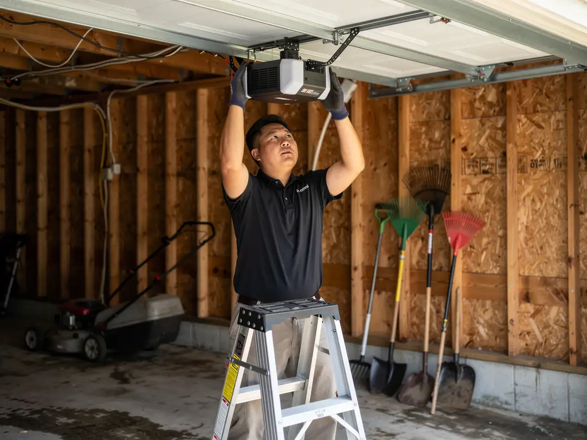 A technician on a ladder installs a garage door opener.